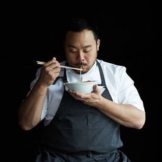 a man in an apron eating from a bowl with chopsticks