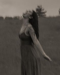 a woman standing in a field with her arms out to the side, looking up at something