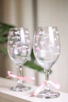 two wine glasses sitting on top of a white shelf next to each other with pink bows