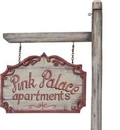 a sign that says pink palace apartments hanging from a wooden pole with chains attached to it