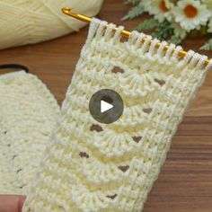 a hand holding a crocheted white object on top of a wooden table next to flowers