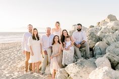 a family posing for a photo on the beach with rocks and water in the background