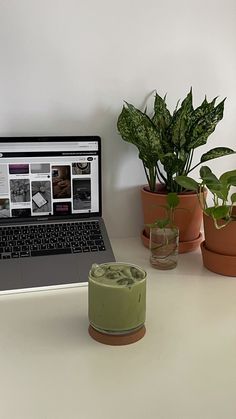 an open laptop computer sitting on top of a white desk next to potted plants