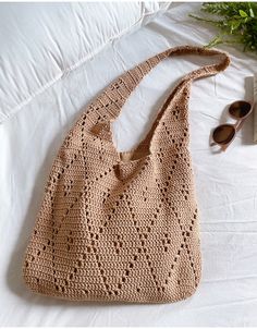 a crocheted purse sitting on top of a bed next to sunglasses and a book