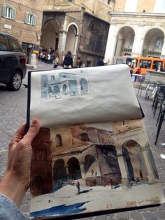 a person holding up an open book in front of a street with cars and buildings