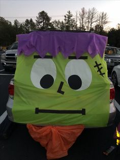 a large green and purple costume sitting on the back of a car in a parking lot