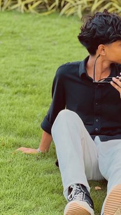 a woman sitting on the grass with her cell phone up to her ear and wearing headphones