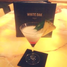 a white oak cocktail in a martini glass on a table with a black box behind it