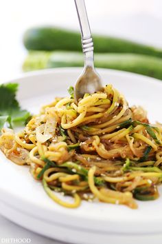 a white plate topped with noodles and vegetables next to cucumber wedged in the background