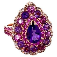 This ring has a deep purple Pear Cut Amethyst that weighs 0.87 Carats and is embellished with 14 Purple Garnets and Amethysts that weigh a total of 1.65 Carats as well as 42 Pink Sapphires that weigh 0.83 Carats. There are also 44 Round Cut Natural Diamonds that weigh 0.22 Carats. The total carat weight of the ring is 3.57 Carats. The ring is crafted in 14 Karat Rose Gold and weighs approximately 5.7 grams. The ring is a size 7 and can be re-sized at no additional charge. Rose Gold Cocktail, Amethyst Cocktail Ring, Sapphire Cocktail Ring, Rose Gold Flower, Pink Sapphire Ring, Diamond Fashion Rings, Gold Cocktail Ring, Gold Cocktail, Diamond Cocktail Rings