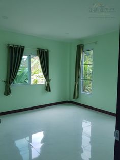 an empty room with two windows and curtains on the window sill, in front of a green wall