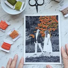 two hands holding up a photo with yarn and scissors on the table next to it