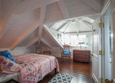 an attic bedroom with a bed, dresser and chair in it's center area