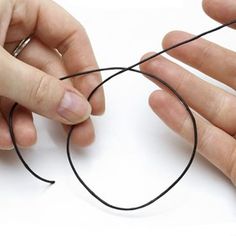 two hands are holding black thread in the shape of a heart