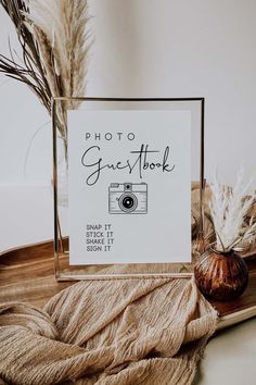 a photo frame sitting on top of a wooden table next to dried plants and a vase