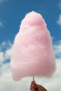 a hand holding a pink cotton candy on a blue sky background with clouds in the background