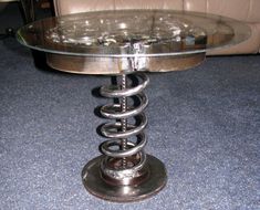 a glass table with metal spirals on the top and bottom sitting on blue carpeted flooring