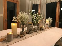 a table topped with lots of candles and vases filled with flowers next to windows