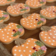 decorated pumpkin cookies sitting on top of a wooden tray with white polka dot dots and pink flowers