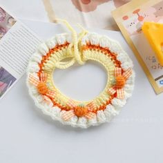 an orange and white crochet bracelet on top of a table next to a book