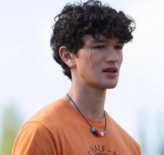 a young man with curly hair wearing an orange t - shirt and beaded necklace