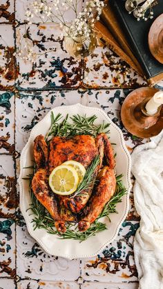 a whole chicken on a plate with lemon wedges and rosemary garnishes