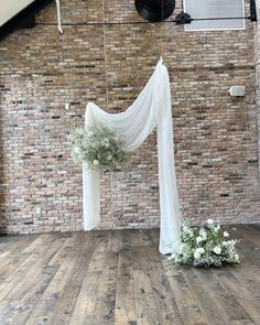 a white drape draped over a wooden floor in front of a brick wall with flowers