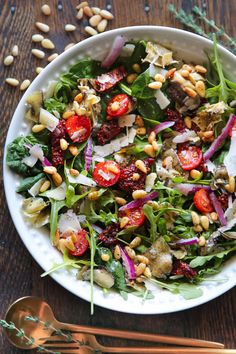 a white bowl filled with salad and dressing on top of a wooden table next to a spoon