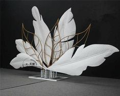 a sculpture made out of white paper with gold leaves on the top and bottom, in front of a black background