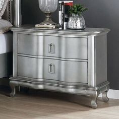 a silver dresser sitting on top of a wooden floor next to a lamp and a bed