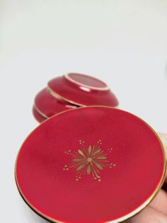 a hand holding a red plate with gold designs on the front and sides, in front of three other plates