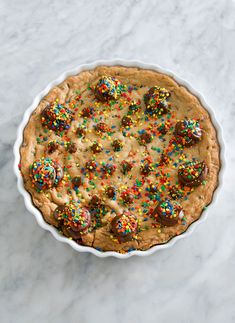 a cookie pie with sprinkles and chocolate covered cookies on the top is sitting on a marble surface