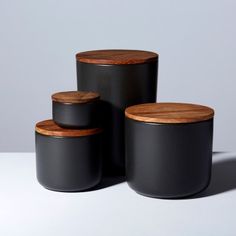 three black canisters with wooden lids on a white surface