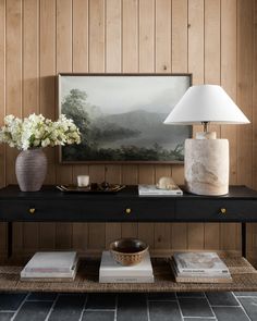 a table with two vases and a lamp on it in front of wood paneled walls