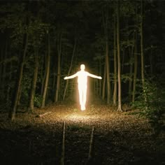 a person standing in the middle of a forest with their arms spread out and lights shining on them