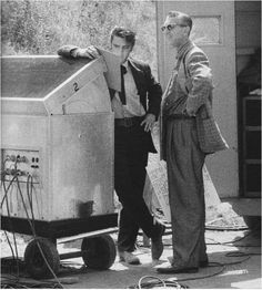 two men standing next to an old fashioned washing machine