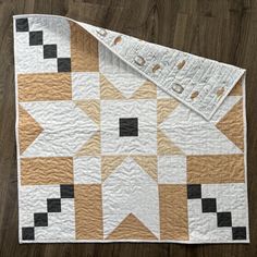 a white and brown quilt on top of a wooden floor with a ruler next to it