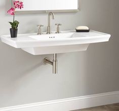 a white sink sitting under a mirror next to a vase with pink flowers in it