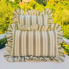 two striped pillows sitting on top of a white table next to some trees and bushes