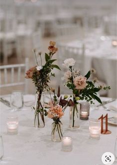 flowers in vases sitting on top of a table next to candles and place cards