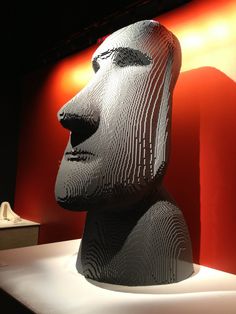 a statue made out of legos on display in front of a red and white wall