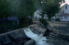 there is a small waterfall coming out of the side of a river with houses in the background