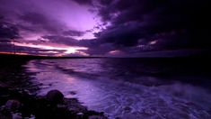 the sun is setting over the ocean with dark clouds and waves crashing on the shore