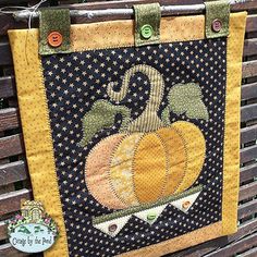 a quilted pumpkin hanging on the side of a wooden bench next to a sign