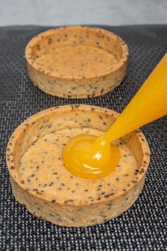 an orange liquid is being poured into two small bowls with black speckles on them