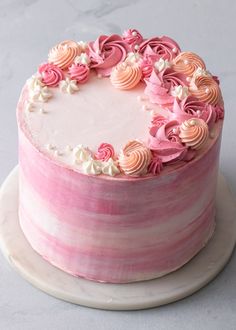 a pink and white striped cake with flowers on the top is sitting on a plate