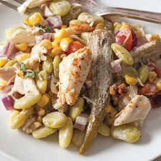 a white plate topped with chicken, corn and tomato salad next to two silverware