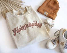 Homebody's unite Live your best lounge life in this cozy crew neck sweatshirt. It is sure to keep you feeling all warm and fuzzy all season long. Beige Letter Print Sweatshirt For Loungewear, Cream Letter Print Sweatshirt For Loungewear, Trendy Cream Sweatshirt For Loungewear, Trendy Cream Sweatshirt, Cute Sweatshirt Designs, Homebody Shirt, Beige Sweatshirt, Market Ideas, Womens Sweatshirts