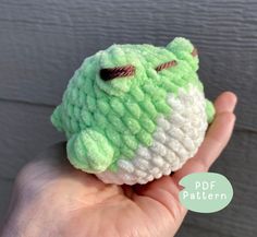 a hand holding a small crocheted green and white stuffed animal in it's left hand