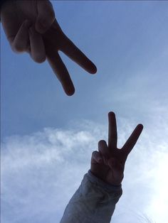 two hands making the peace sign with their fingers in front of blue sky and clouds